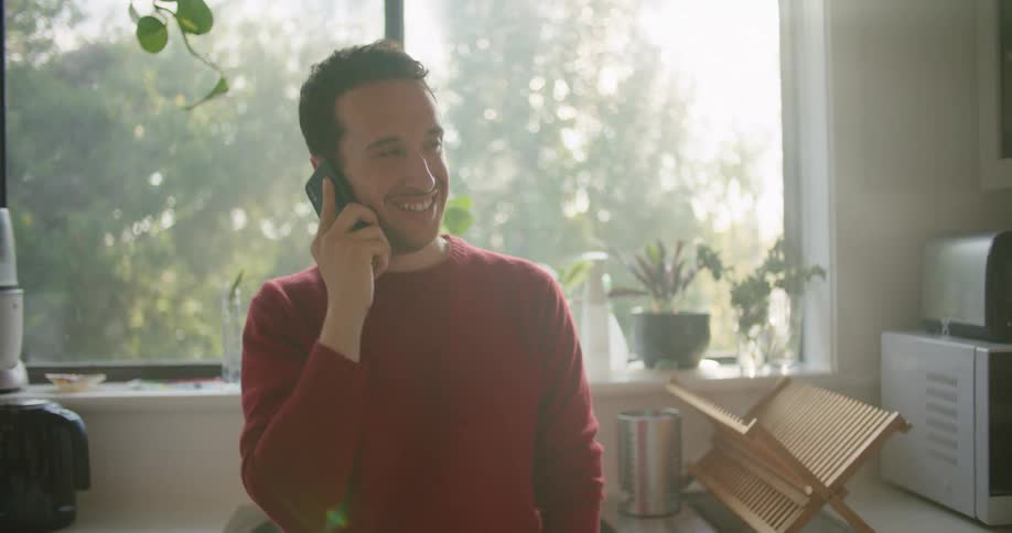 Young man talking on the phone while standing on the kitchen at home in the morning