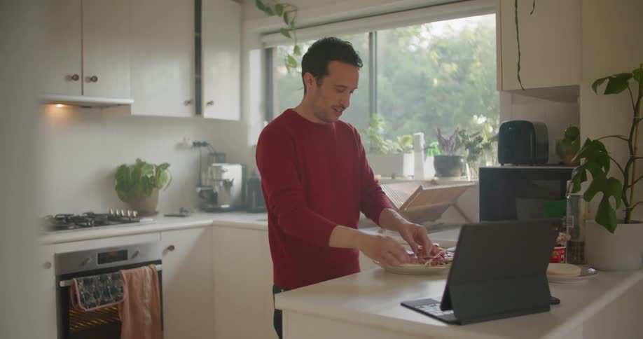 Young man cooking food on the kitchen at home while talking on a laptop