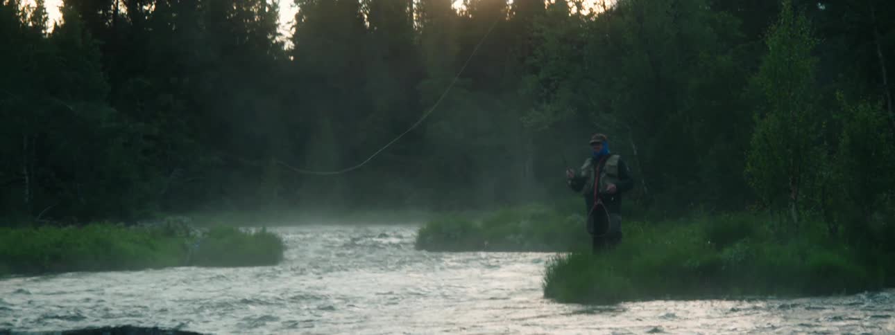 A man stands on the shore and casts his fishing line in to the water