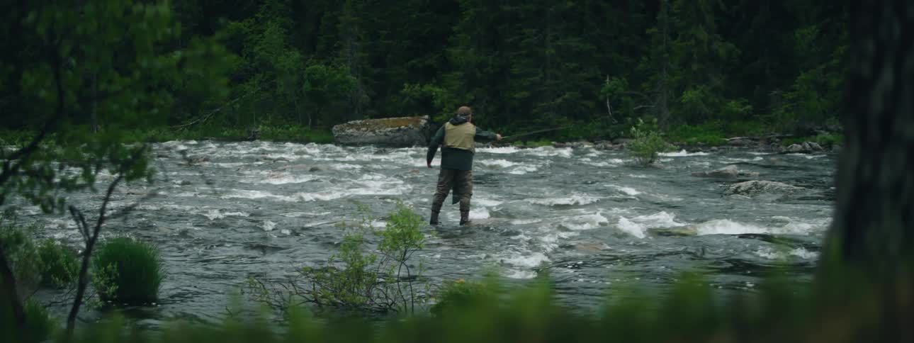 A man stands in a river casting his fishing line as the water flows around him