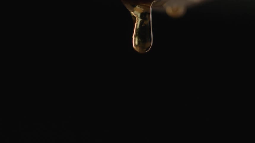Translucent amber drop falls leaving long connect tendril that finally snaps against black background