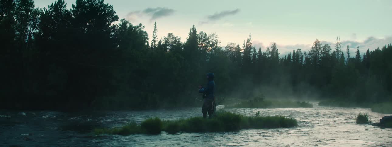 Man standing on a small grass islet on a river in the woods fishing in the morning