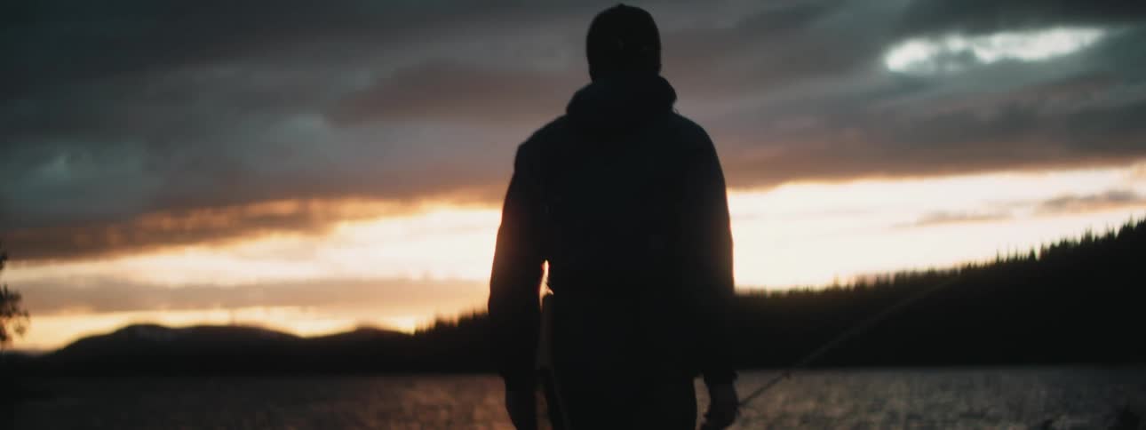 A man is walking towards the lake with a net and fishing pole