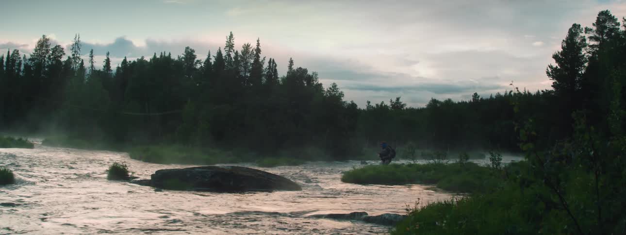 A person stands on the shore of a river and gets fishing rod ready