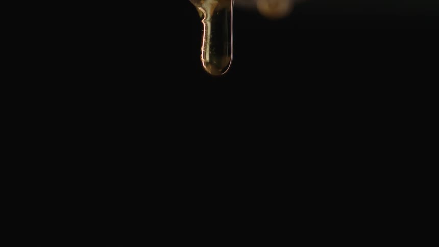 Strand of thick honey dripping against a black background