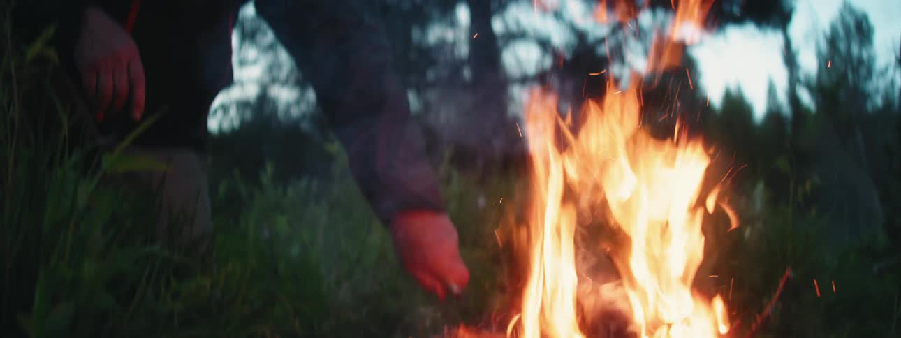 Couple of friends stoking the fire on a campfire in the forest at morning