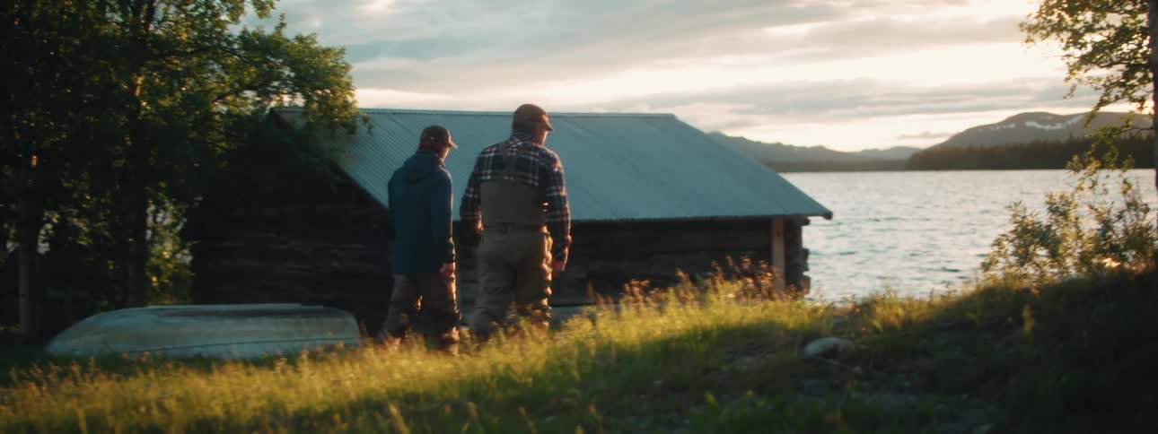 Two men walk on the grass towards the lake