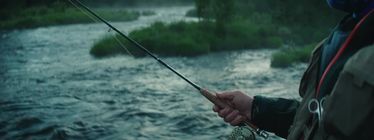 A man casts a fishing line into a fast moving river