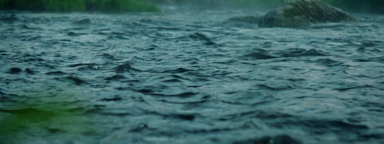 River water flows past rocks as rain falls