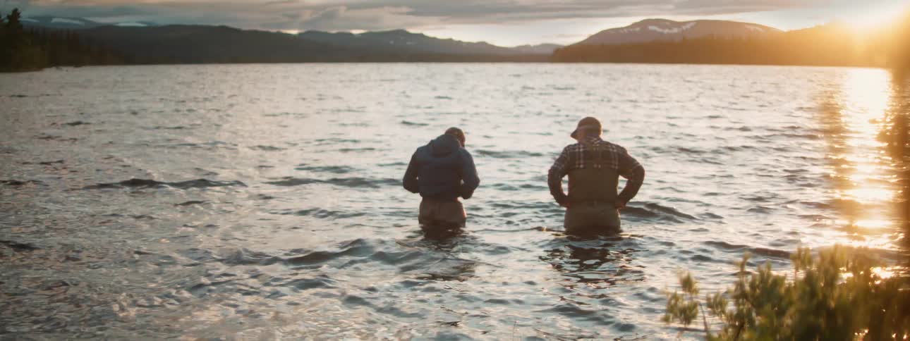 Two men standing on a lake in the mountains at sunset