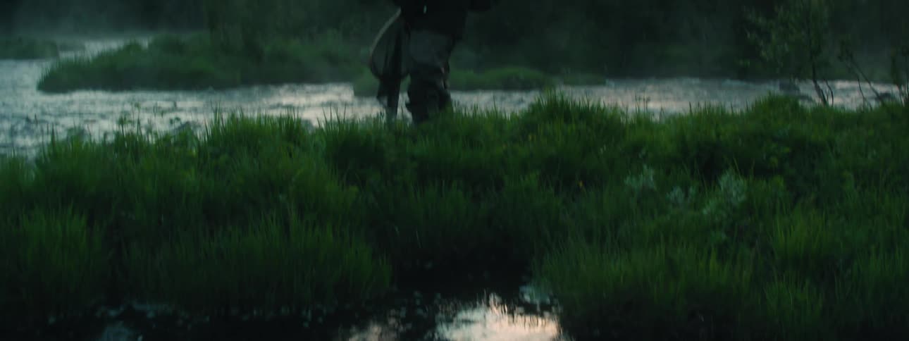 Man standing on the grass near a river fishing at sunset