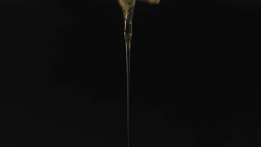 Strand of dripping honey pouring down against a black background