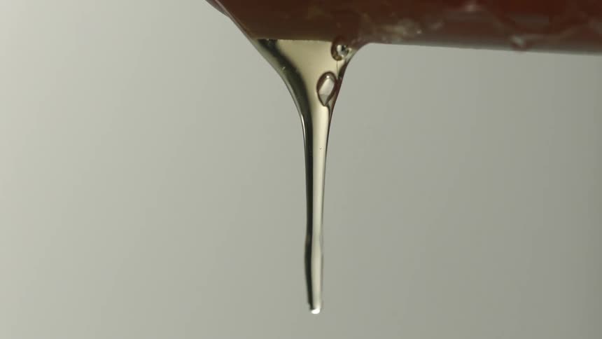 Amber syrup drips from utensil against pale gray background