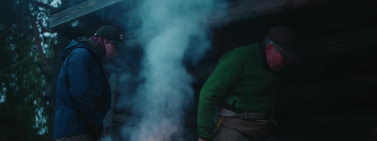 A man walks over to the bonfire and zips his jacket up