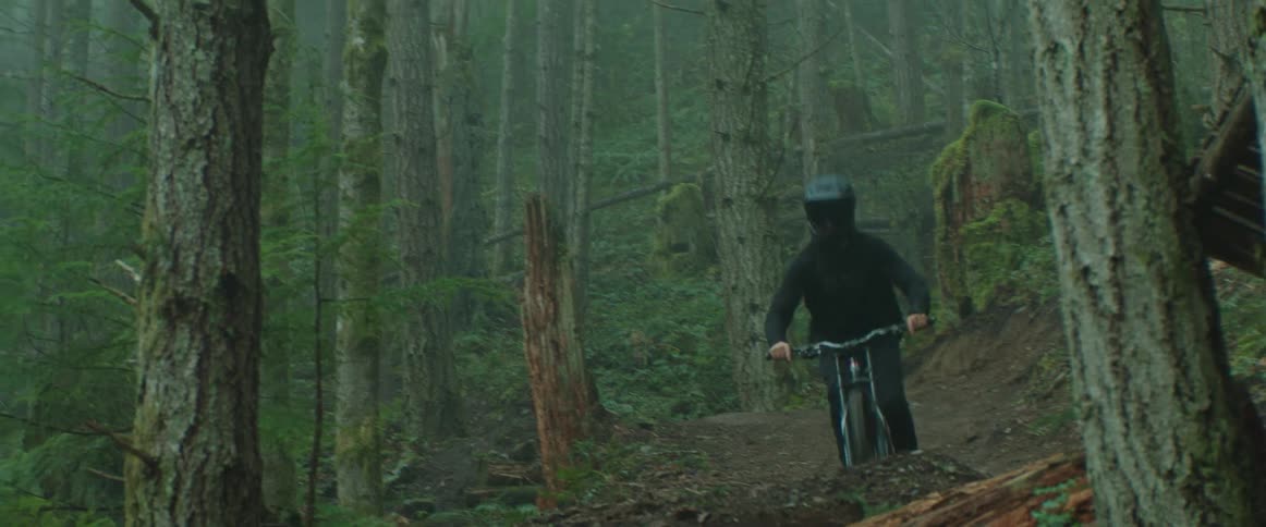 A man on a mountain bike speeds down a trail and hits a jump