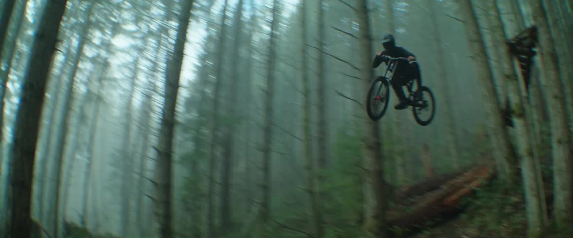 A mountain biker jumps by the camera on a foggy day in the forest