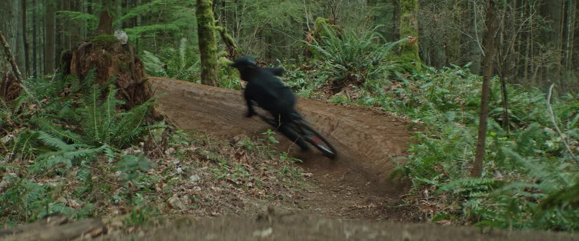 A person on a mountain bike speeds through a dirt corner on a forest trail
