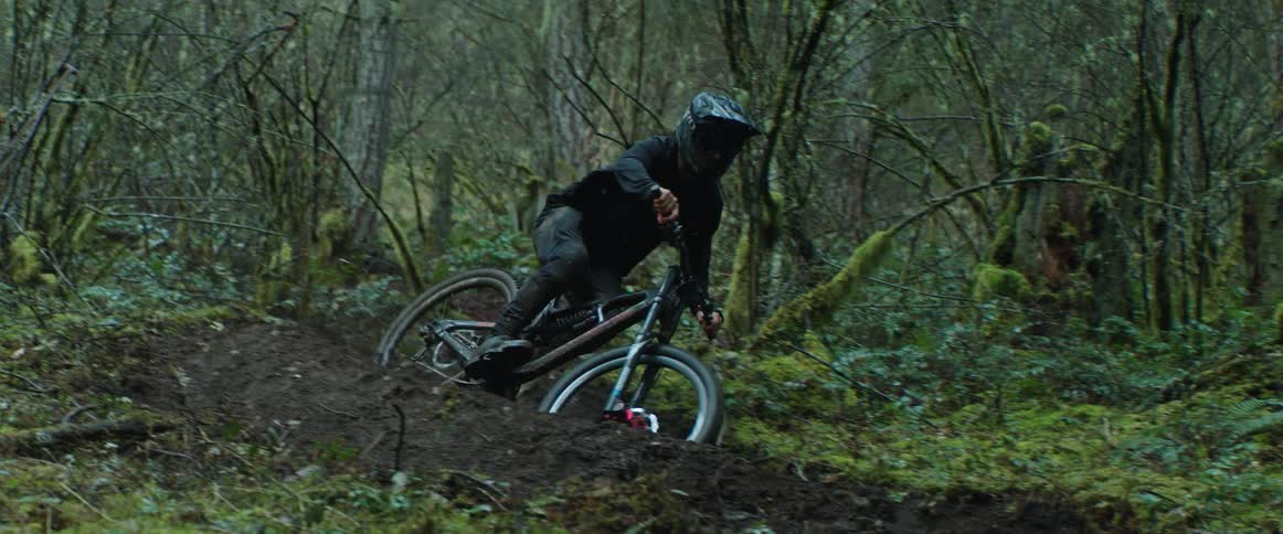 A mountain bike athlete weaves through tight muddy corners in the forest