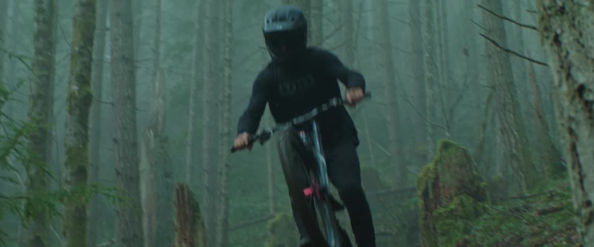 A mountain bike rider hits a jump on a forest trail and flies near camera