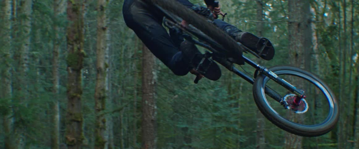 A man whips his mountain bike through the air off a large forest jump