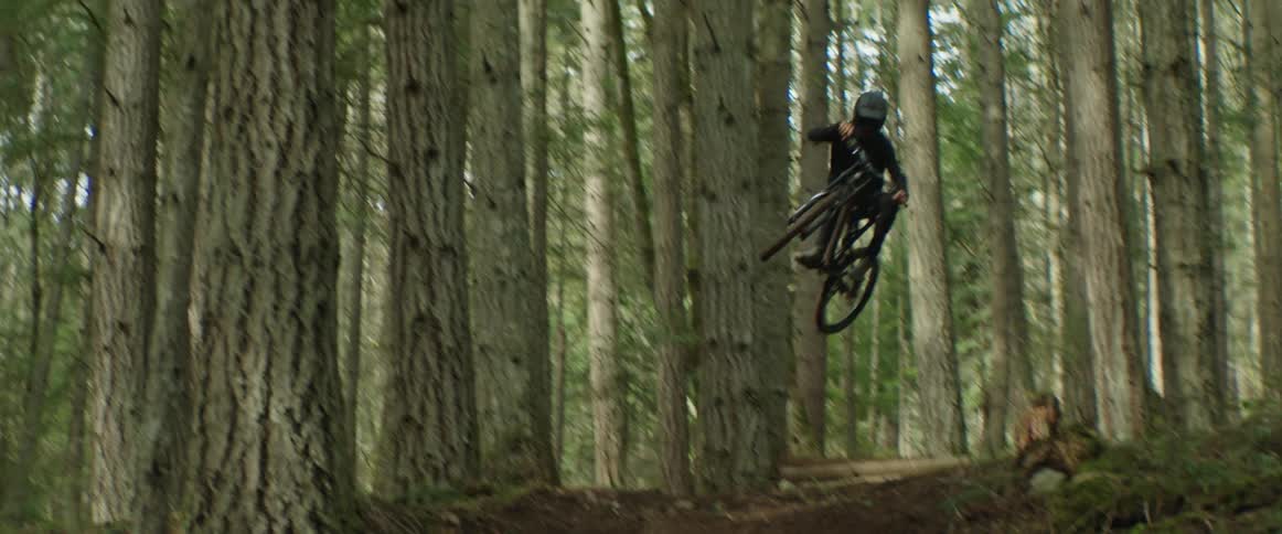 A mountain bike hits a large trail jump while riding a fast forest trail