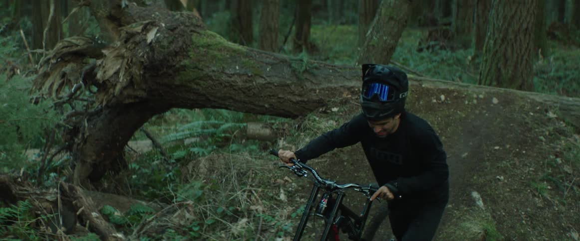 A man with a helmet pushing a bicycle up a forest trail