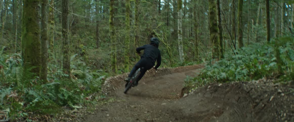 Person rides mountain bike through high-speed trail corners in the forest