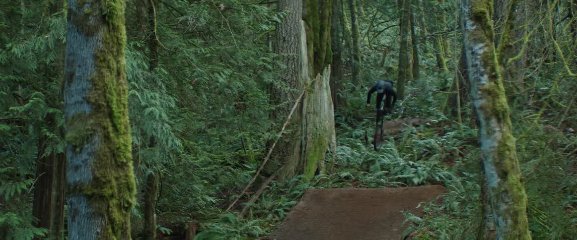 A man performs a backflip trick on his bike in a lush forest