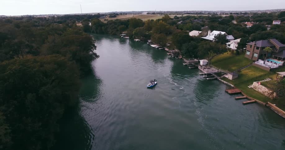 A fishing boat sits in the middle of a river with houses on one bank