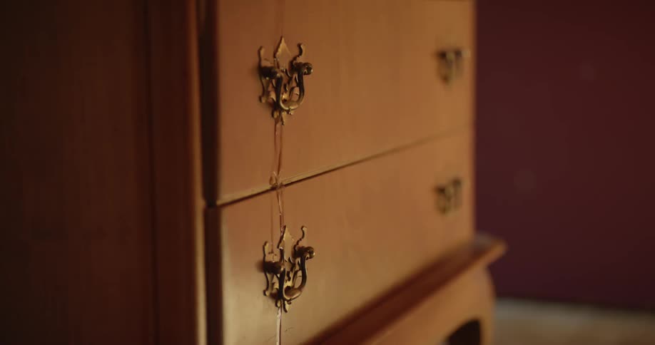 Water flows down past drawer pulls on dresser drawer in room with maroon walls