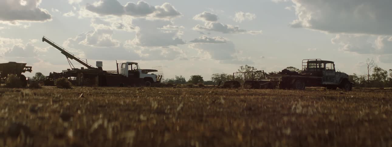 A child riding a bicycle by trucks in a rural field