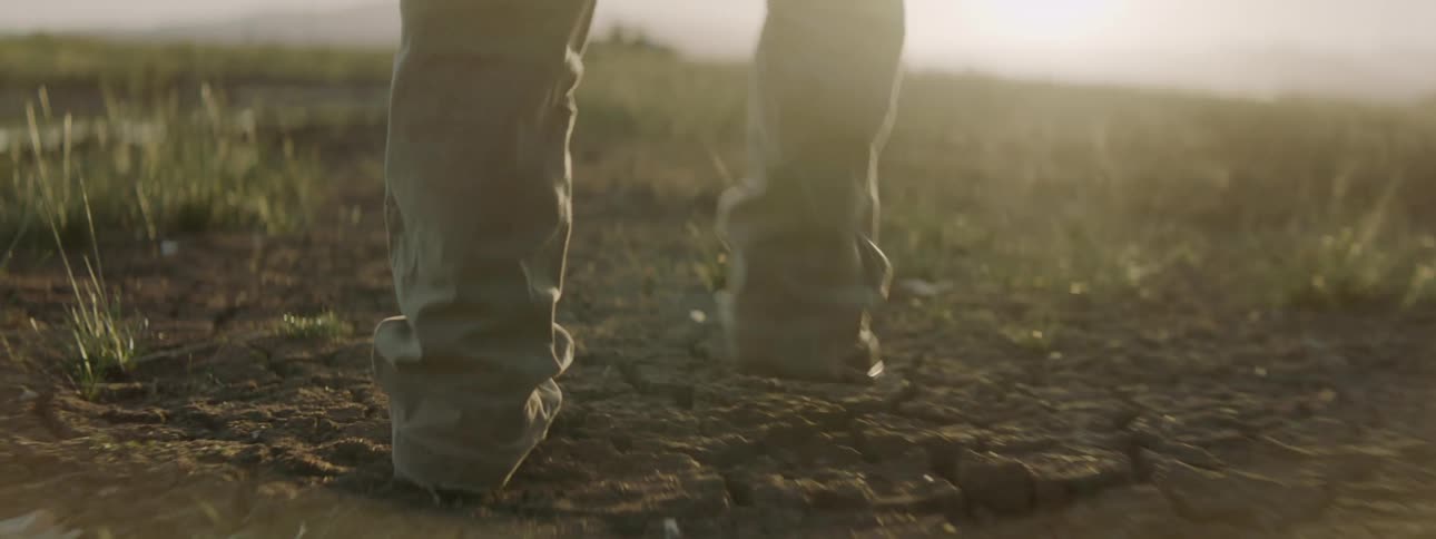A man in jeans and boots walks through an open field