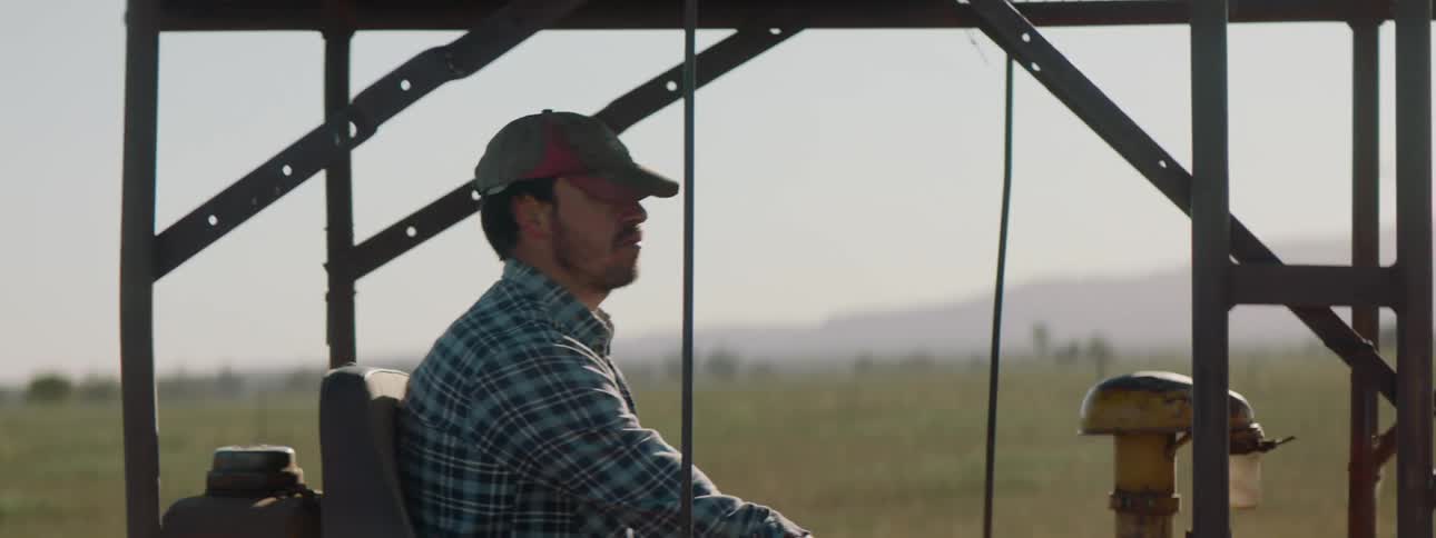 A man is on a tractor in a field operating the gears