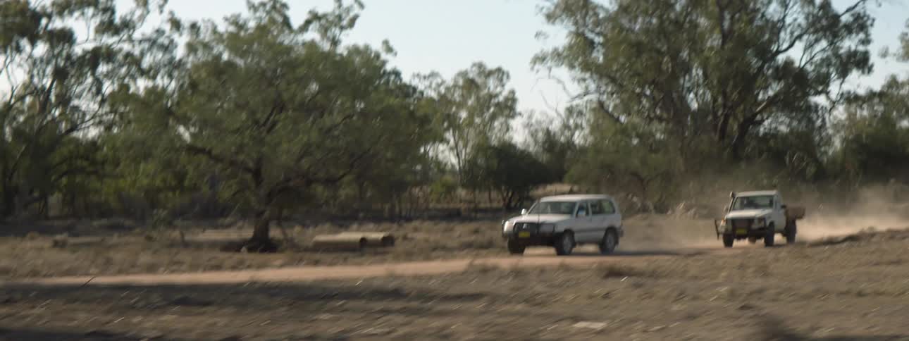 A small truck passes a vehicle on a dirt road