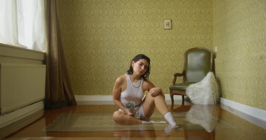 A woman sits on a rug on the floor of a flooding room