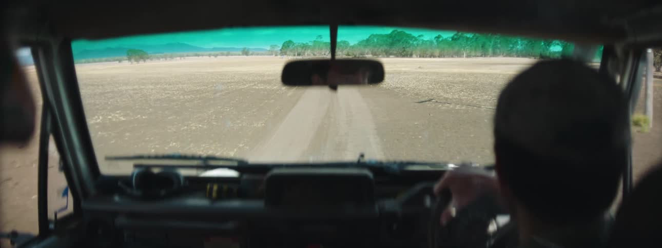A man is driving a car on a dirt road in a rural area