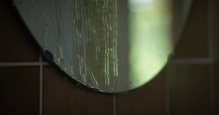 Water flows down circular mirror sitting against tiled wall and reflecting light