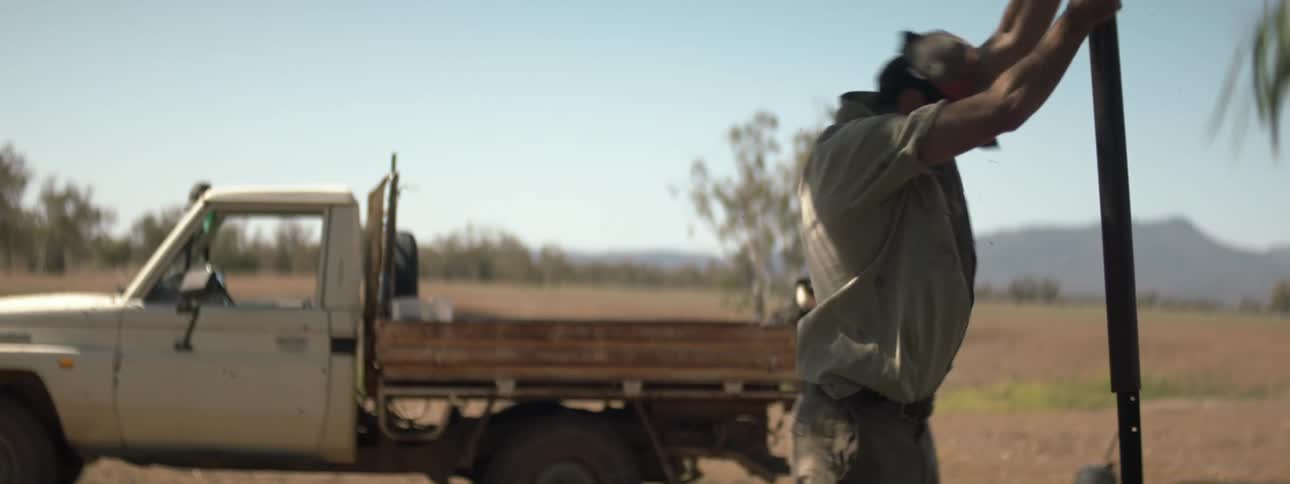 A man uses a metal pipe over a metal pole to plant the pole in an open field
