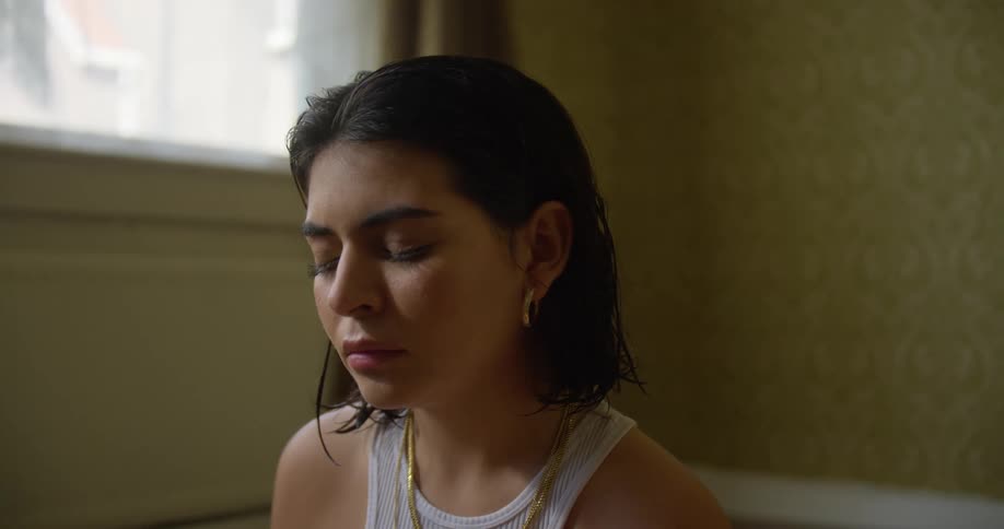 A woman with necklaces in a room with a wall and window in the background