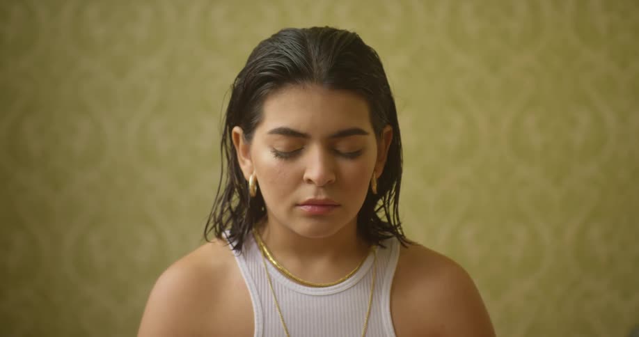 A woman meditates in a tank top and gold jewelry