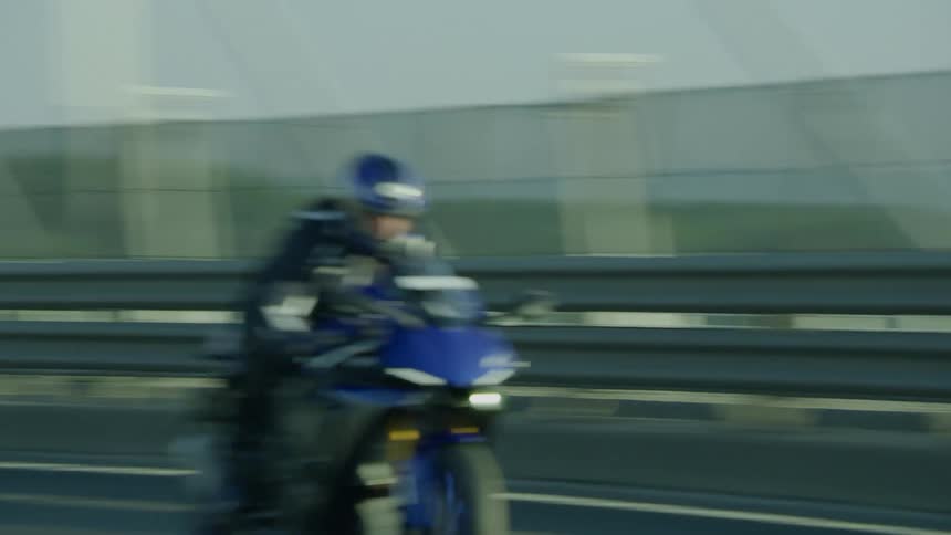 A motorcycle with electric blue trim travels on a bridge with other traffic
