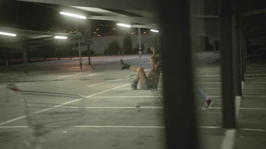 A man is pushing a car through a lot with a woman in it