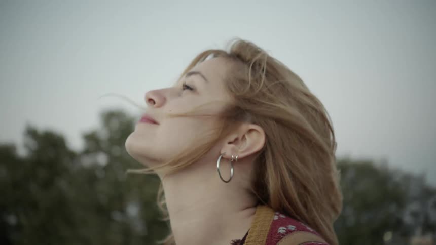 A woman looks up at a cloudy sky on a windy day