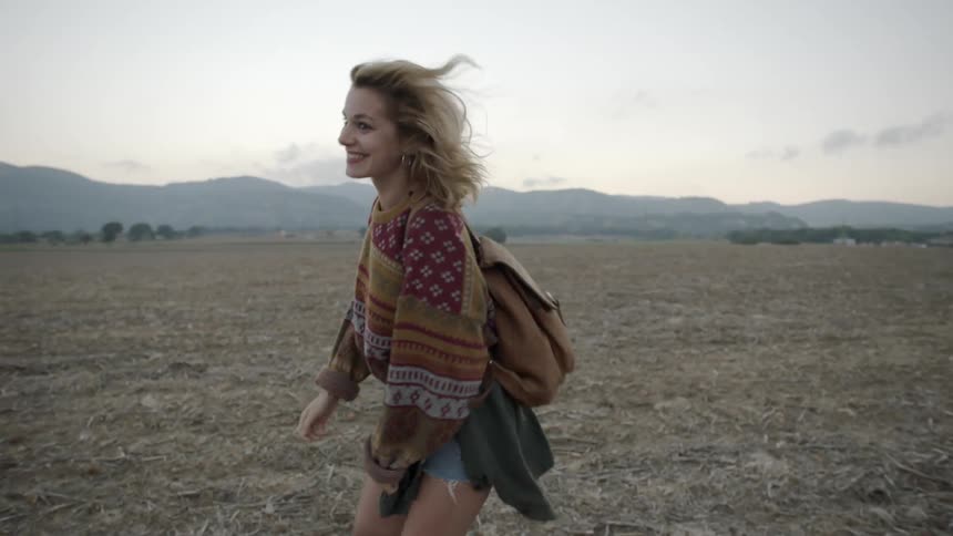 A woman runs over a windy field before turning around smiling