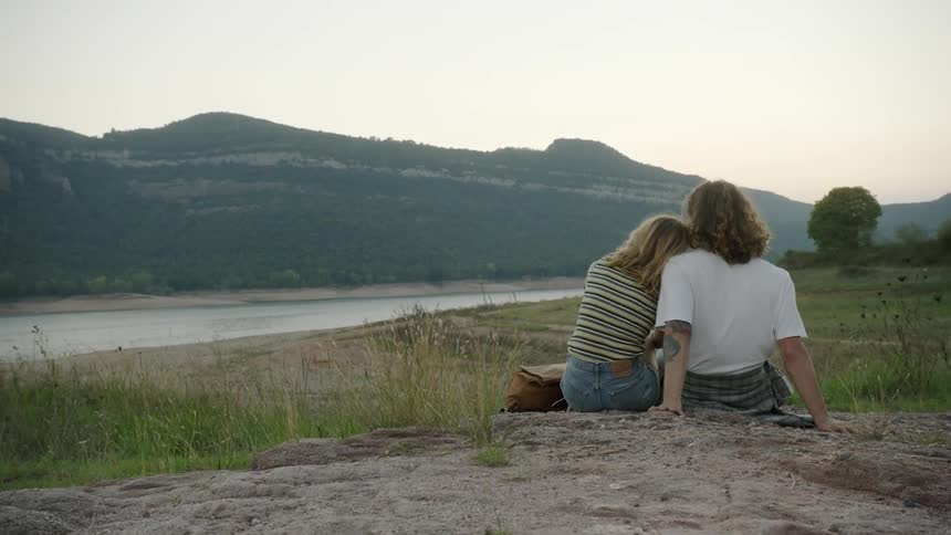 A man and woman sit near a river and mountain