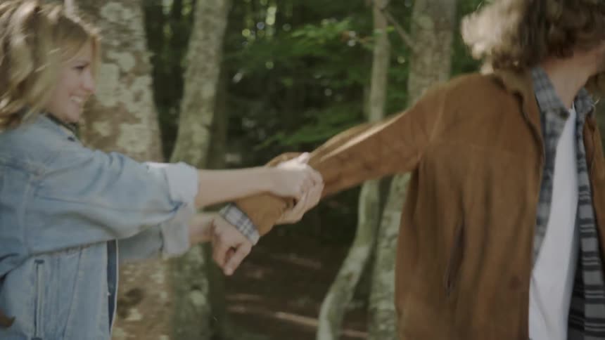 A man and women walk holding hands and playing in the woods