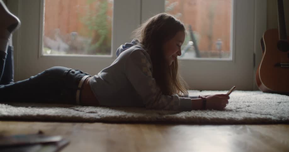 A girl is laying on the floor on a rug looking at her cellphone