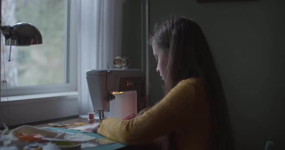 A young woman is sitting at a desk using a sewing machine