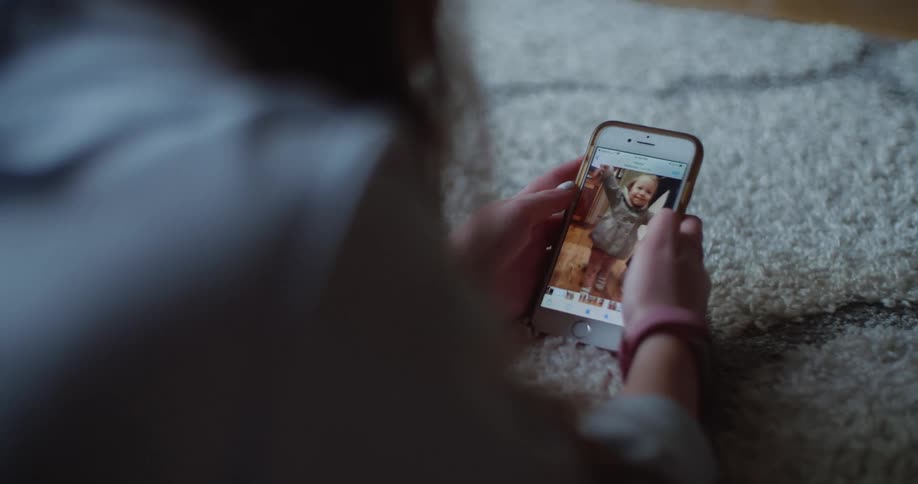 A woman laying on a rug on a floor while looking at a smart phone