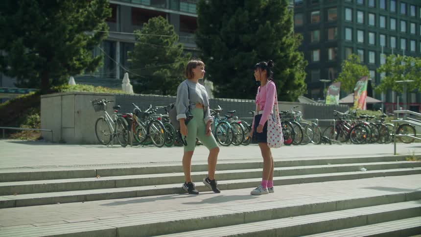 A pair of young women greet one another by bumping fists and sharing a hug before they begin to chat